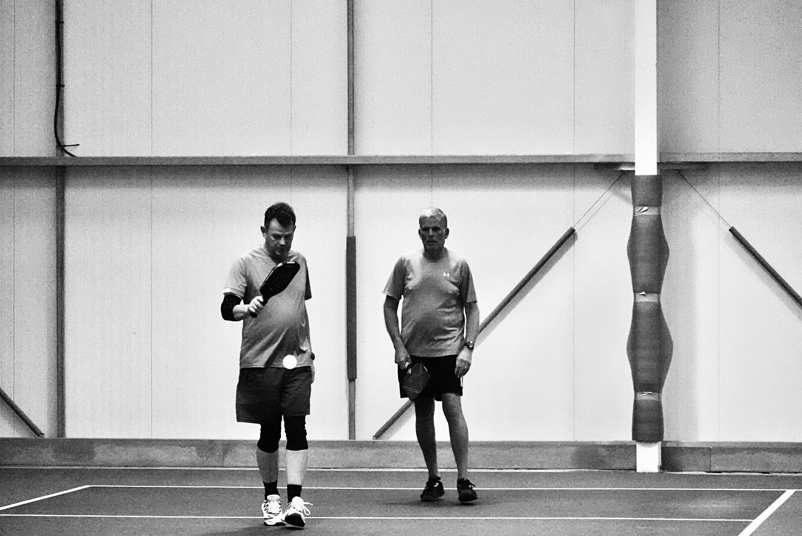 A player bending low for a backhand pickup on a blue indoor court.