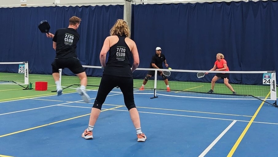 Two pairs rallying across the net during an indoor doubles match.